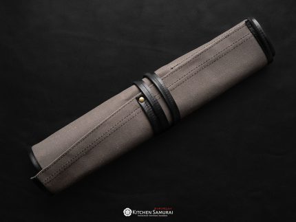Open grey canvas knife roll with black leather trim, six slots and a zipped accessory pouch, displayed with knives on a wooden surface